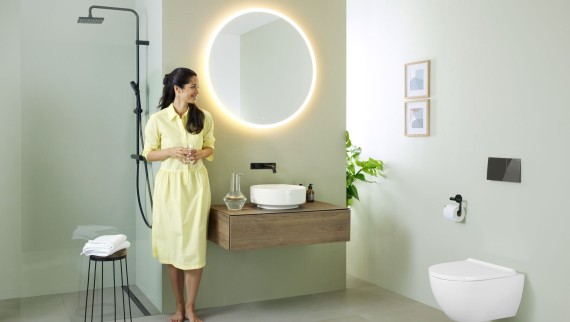 Woman in yellow dress standing in front of mint green bathroom with furniture and bathroom ceramics from Geberit and black taps